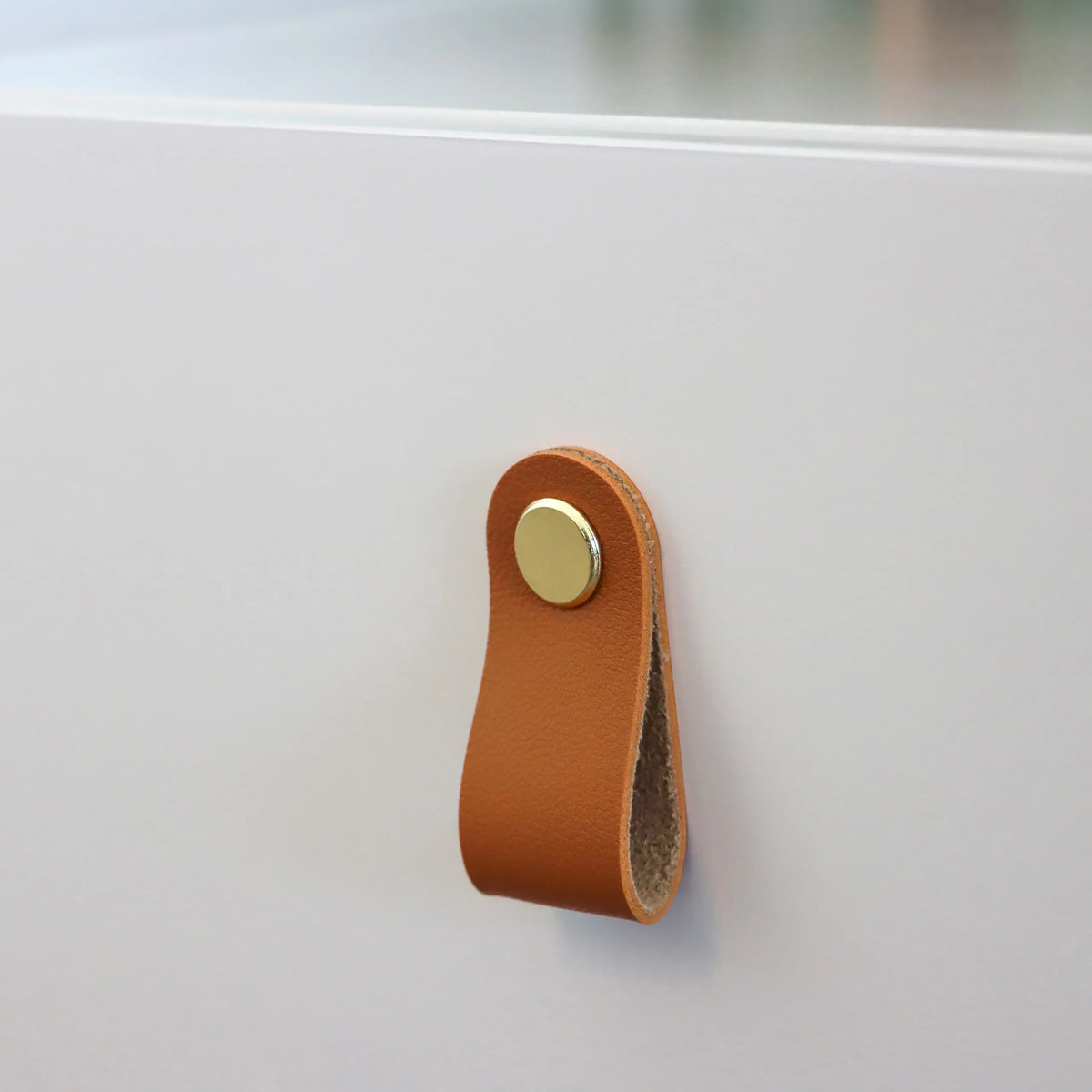 Bruine lederen handgreep met goudkleurige knop aan de witte bijzettafel TAROLO III van hjh LIVING