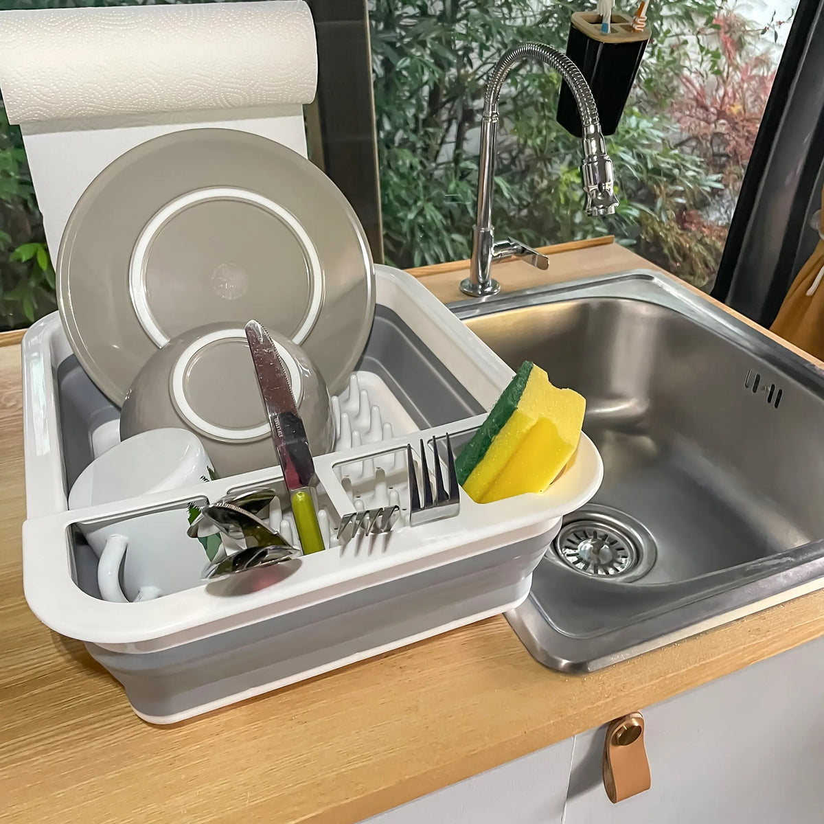 Grijs-witte opvouwbare bak CLEAN SIL als afdruiprek met servies en spons naast een spoelbak van hjh OFFICE