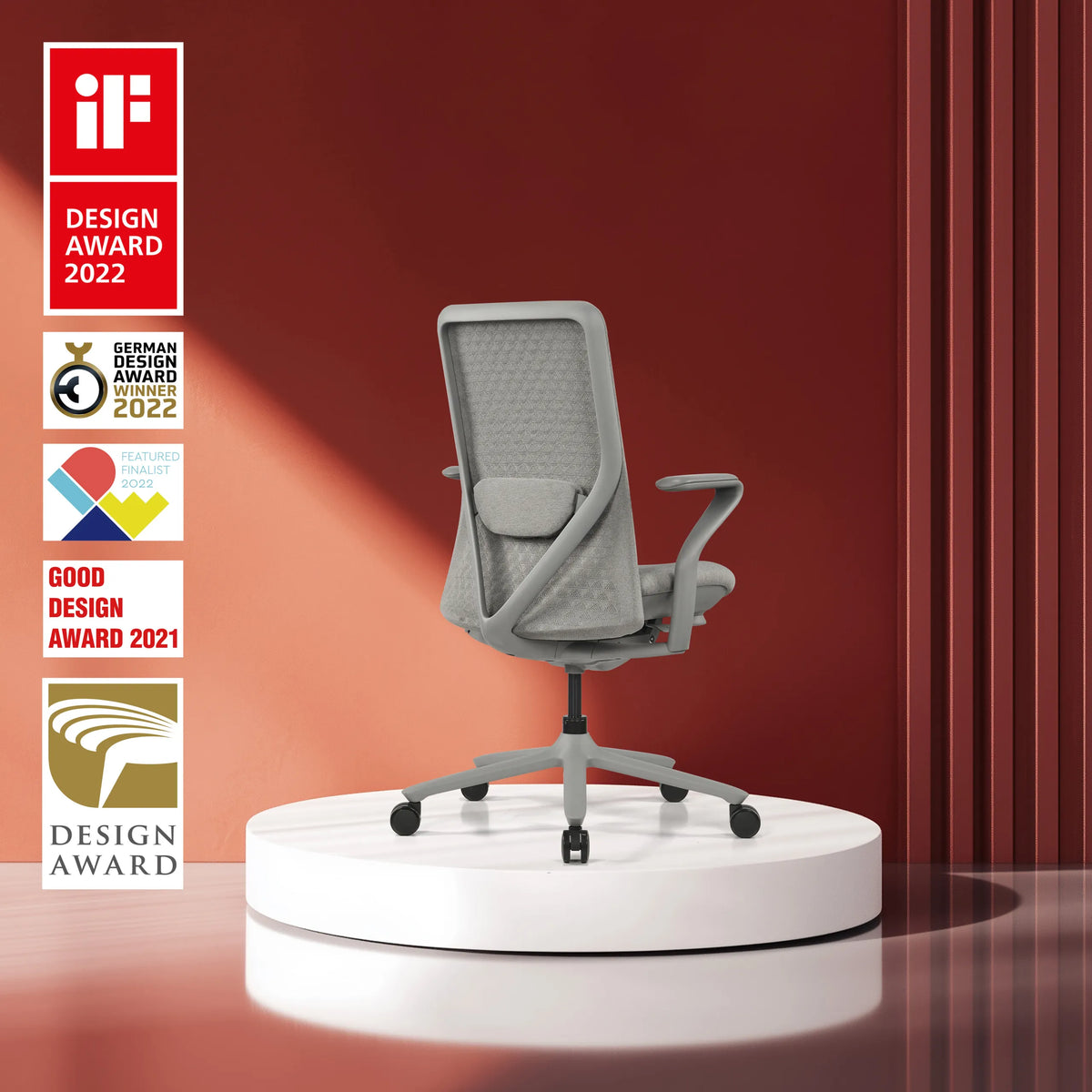 Grijze high end bureaustoel VERVIO met netrugleuning op een wit platform tegen een rode achtergrond van hjh OFFICE
