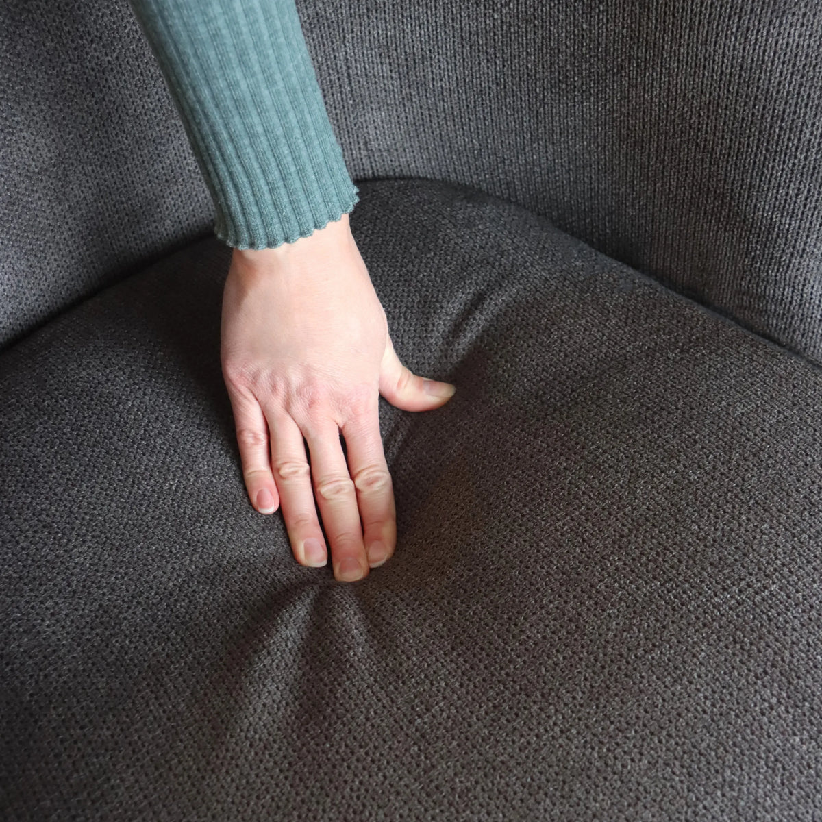 Grijze stoffen bekleding van het zitvlak van de HAYRIVER lounge bank onder een hand van hjh LIVING
