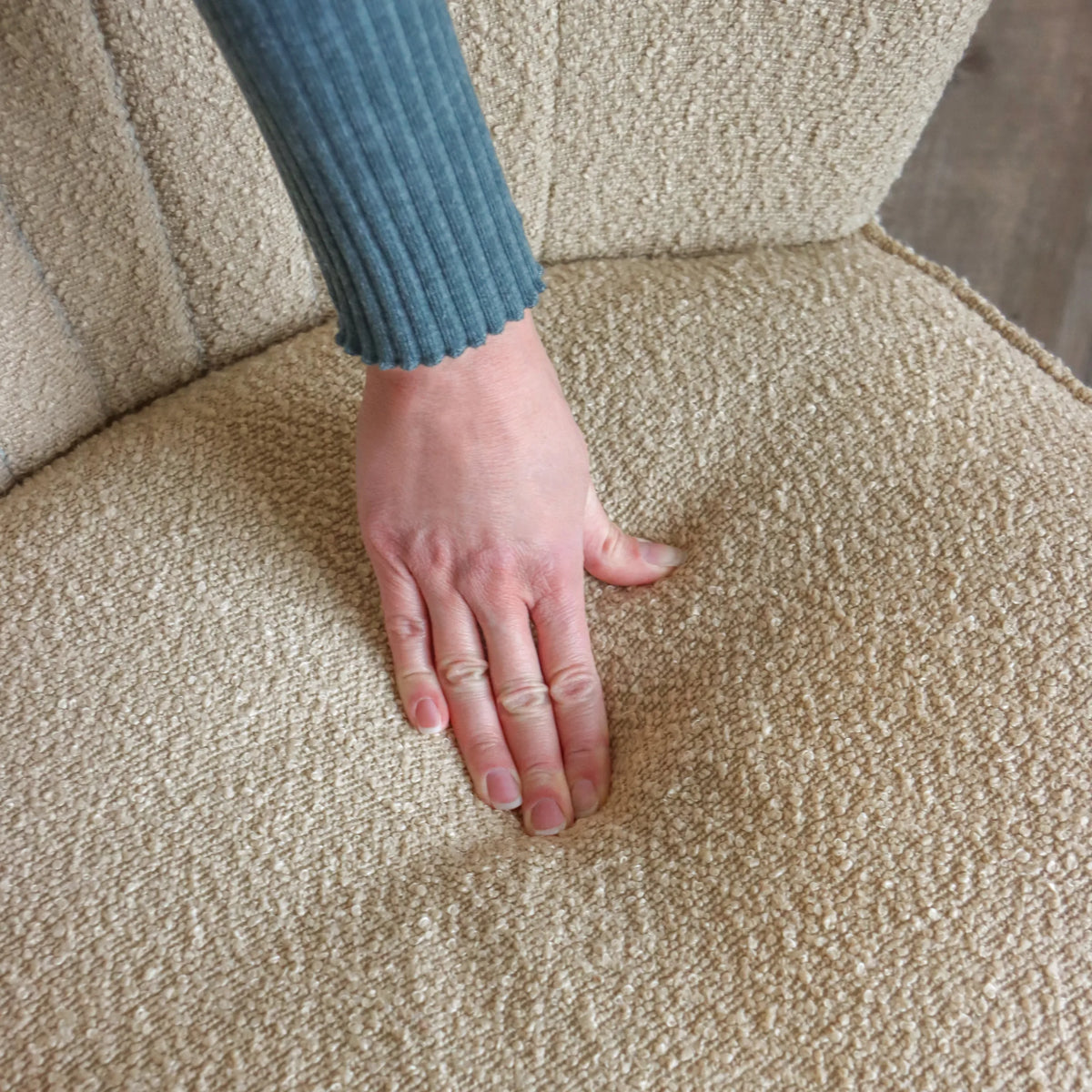 Beige structuurstof van de MANISO lounge stoel met een hand op het zitvlak van hjh LIVING