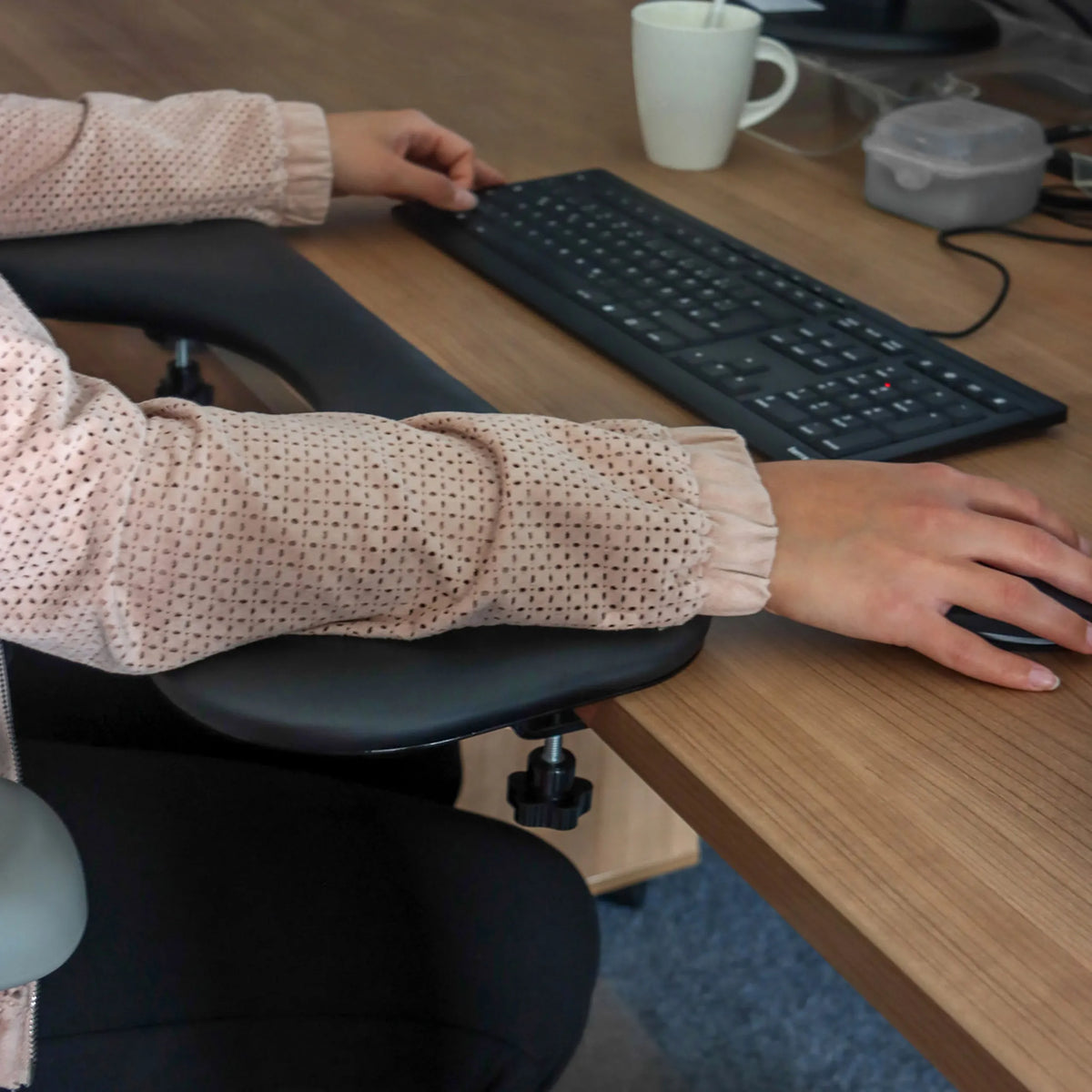 Zwarte armleuning van het model RELEX RT2 aan een bureau met toetsenbord en muis van hjh OFFICE