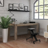 Zwarte ORTHONI kniekruk op wieltjes voor een houten bureau in een lichte kamer van hjh OFFICE