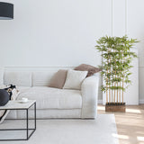 Groene Kunstplant BAMBUS I in een houten pot naast een witte bank van hjh OFFICE