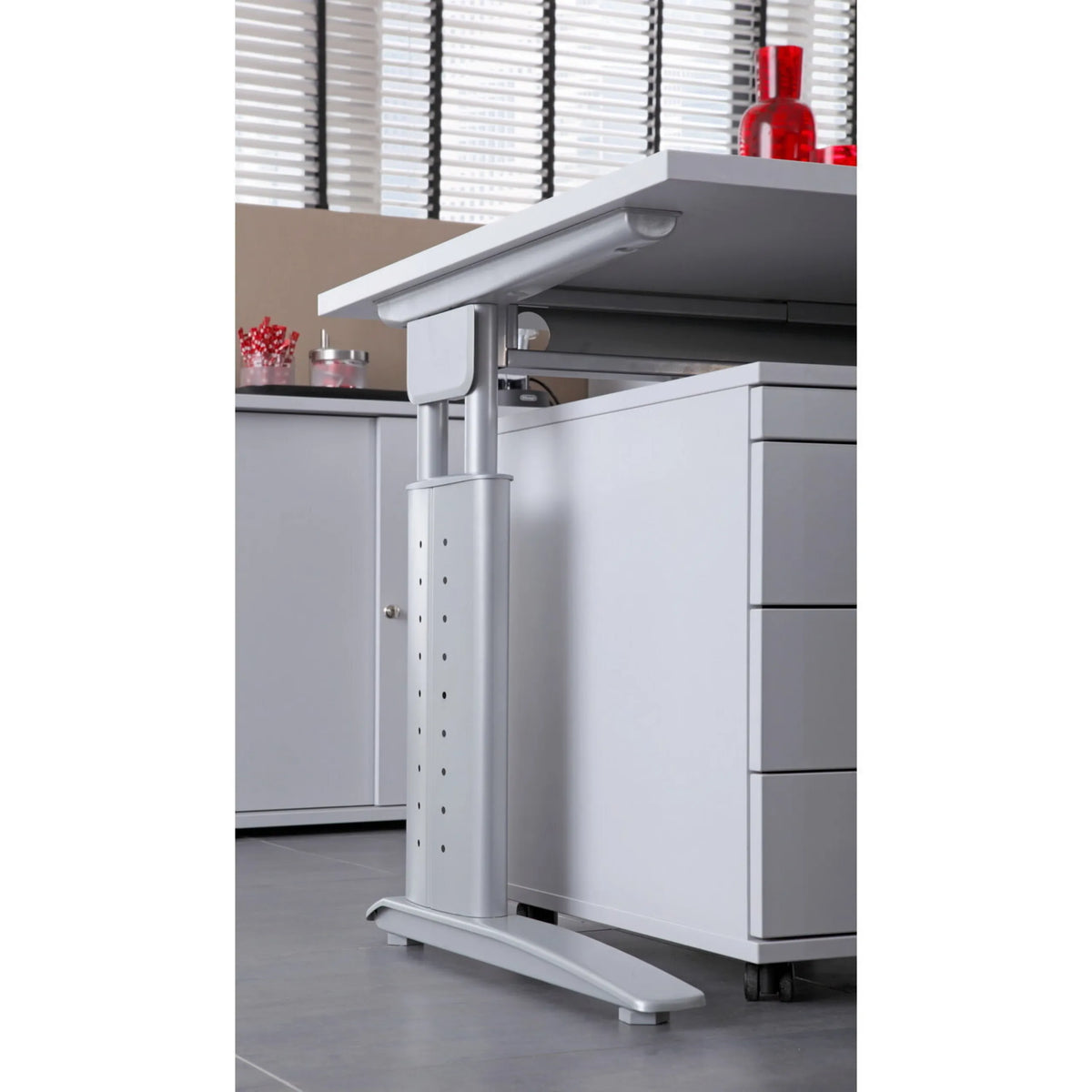 Höhenverstellbares Tischbein des Schreibtischs UNDA 12 S in Grau-Silber neben einem Rollcontainer von hjh OFFICE PRO